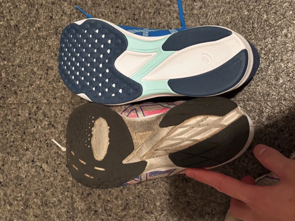 上下に並べられた2足のランニングシューズの靴底。上は青と水色の新品に近いアシックスシューズで、下は白とピンクのアシックスシューズで、特に踵やつま先が摩耗し汚れが見られる。