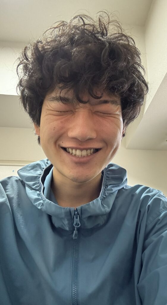 青いフード付きジャケットを着た筆者Tomoyaさんが、目を閉じて満面の笑顔を浮かべているアップのポートレート。レース前の高揚感や満足感が伝わってくる。