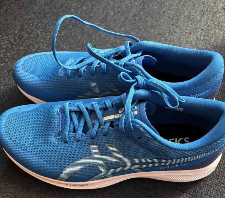 暗い床に並べられた2足の青いランニングシューズ。紐は結ばれており、白と水色のラインが側面に入っているアシックスの製品であることがわかる。