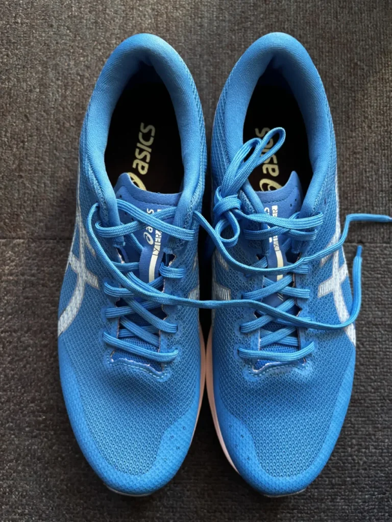 灰色の床に並べられた2足の青いアシックスランニングシューズを上から撮影。靴紐は結ばれており、全体的に清潔で新品に近い状態である。