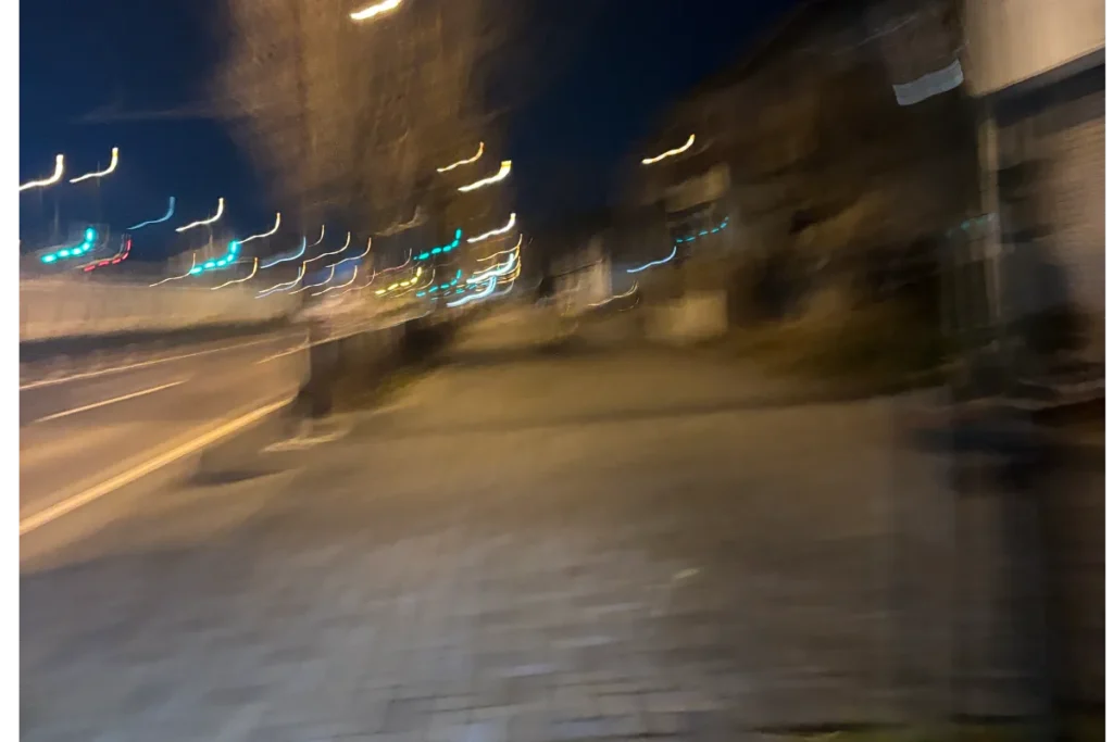 長時間露光で撮影された夜の都市風景。道路を走る車の光が水平方向に引き伸ばされ、建物のシルエットがぼやけて見える。