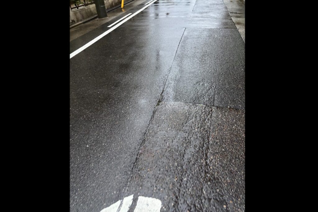 光を反射する濡れたアスファルトの地面と中央の白線。都市の道路風景。