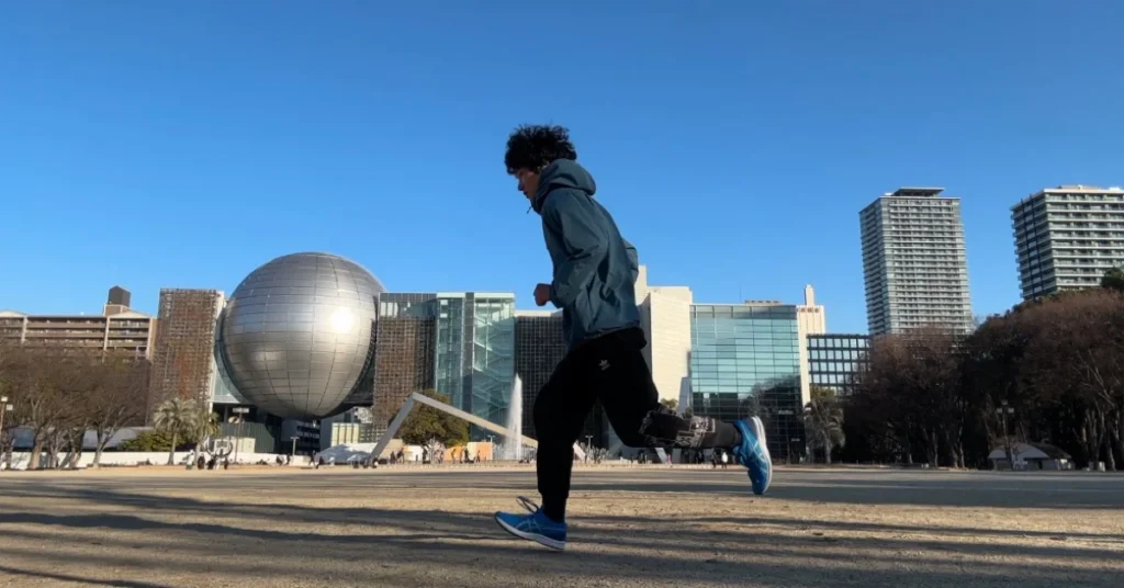 青空の下、球体オブジェクトのある広場で青いランニングシューズを履いて走る男性