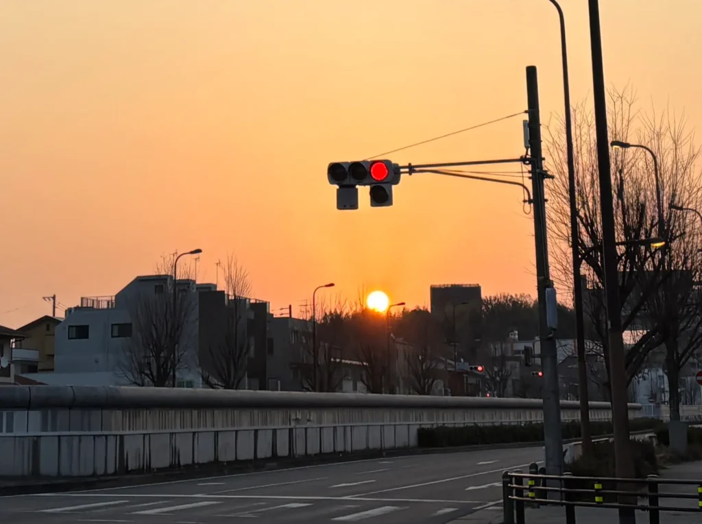 朝焼けのオレンジ色の空を背景に、赤信号と地平線から昇る太陽を捉えた道路風景